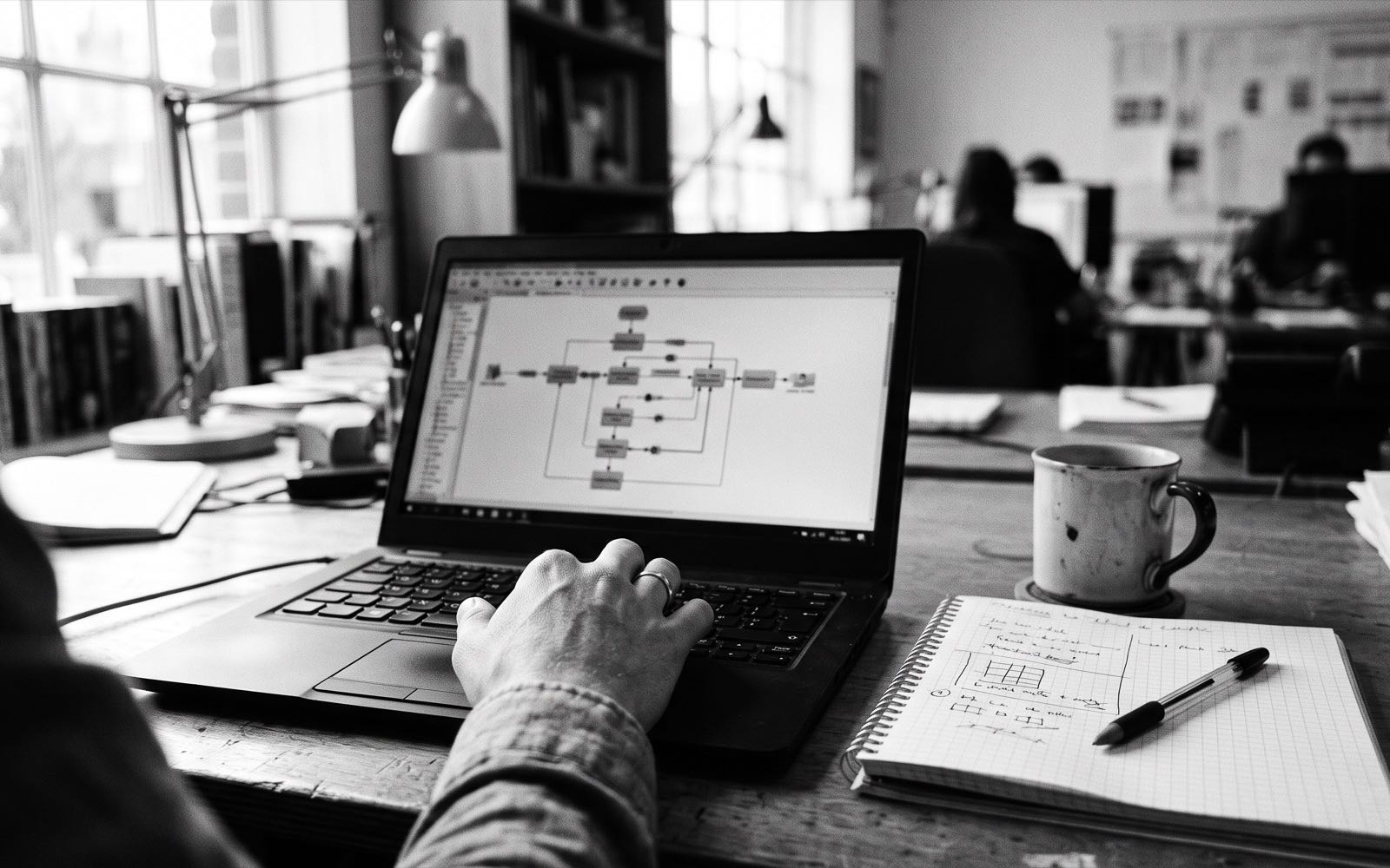 Ofis masasında dizüstü bilgisayar ekranında açık iş akışı şeması, yanında not defteri ve kalem